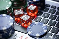 Red dice and poker chips on laptop keyboard with playing cards showing pocket aces, representing online gambling and casino games. Close-up macro shot.