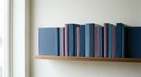 Row of blue and purple hardcover books arranged on wooden shelf against white wall creating minimalist home library display for interior design.