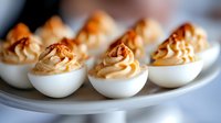 Deviled eggs topped with paprika and creamy filling, arranged on white plate for appetizer, catering, or party food presentation.