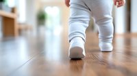 Close-up view of baby feet in white socks taking first steps on wooden floor, shallow depth of field capturing precious milestone moment in child development.