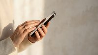 Hands holding smartphone with touchscreen in soft natural light against textured wall background for mobile technology and communication concepts.