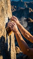 Rock climber hands gripping granite cliff face with chalk dust against mountain landscape background for outdoor adventure sports.