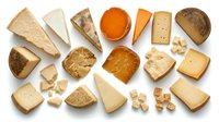 Assorted cheese varieties and bread slices arranged on white background, including cheddar, brie, and whole grain loaf for food styling, culinary content, and gastronomy projects.