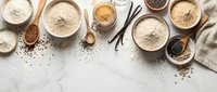 Baking ingredients in wooden bowls on marble surface with flour, spices, vanilla beans and measuring spoons for homemade cooking and recipe preparation.