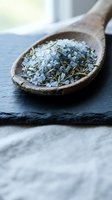 Aromatic herb salt blend with rosemary in rustic wooden spoon on slate surface for gourmet cooking and seasoning applications.