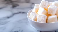 White fluffy marshmallows in ceramic bowl on marble background with copy space. Sweet treats and confectionery concept for dessert recipes and food blogs.