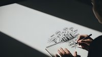 Business person drawing creative strategy plan with lightbulb and gear icons on white paper for startup development and innovation planning.