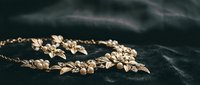 Elegant gold floral jewelry necklace with delicate leaves and pearls on dark fabric background for luxury fashion and bridal accessories.