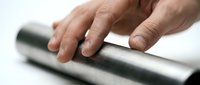 Close-up of a hand touching a polished stainless steel pipe, highlighting industrial metal texture and craftsmanship in manufacturing.