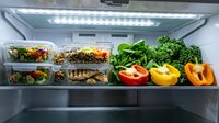 Refrigerator shelf displaying fresh vegetables and prepared meals in containers, including bell peppers, leafy greens, and salads for meal planning and healthy eating.