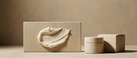 Cream-colored cosmetic product with smooth texture displayed on kraft paper box next to cylindrical and rectangular packaging containers in neutral tones for skincare branding.