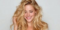 Young woman with tousled blonde hair and natural freckles smiling against neutral gray background, showcasing voluminous hairstyle for beauty advertising.