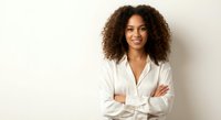 Young African American businesswoman with curly hair smiling confidently with crossed arms in white professional shirt against neutral background.