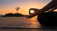 Peaceful meditation at sunset beach with silhouette practicing yoga pose in background. Mindfulness and wellness concept for relaxation and spiritual balance.