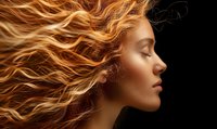 Profile of woman with flowing copper hair against black background, eyes closed with serene expression, highlighting natural beauty and warm golden skin tones.