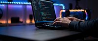 Software developer coding on laptop at night with colorful bokeh lights in background. Programming workspace with hands typing code on computer screen.