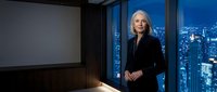 Confident mature businesswoman standing in modern office with city skyline view at night, professional corporate executive in elegant black suit.