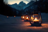 Glowing oil lanterns lined up in snow at dusk, mountain silhouettes in background create cozy winter atmosphere for seasonal outdoor decoration.
