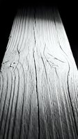 Weathered wooden plank with natural grain patterns and cracks in dramatic black and white lighting for rustic design projects.