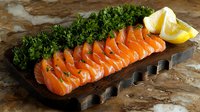 Fresh raw salmon sashimi slices arranged on wooden serving board with bright lemon wedges and fresh parsley garnish on rustic stone background.