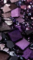 Crushed purple and black eyeshadow palette fragments with metallic shimmer texture creating abstract makeup composition in dark moody lighting.