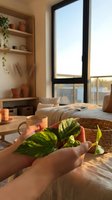 Hands holding fresh green plant leaves in sunlit bedroom with natural morning light streaming through window creating peaceful wellness atmosphere.