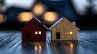 Miniature wooden houses with glowing windows at dusk create cozy atmosphere on dark textured surface. Warm bokeh lights in background add magical ambiance.