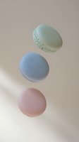 Colorful French macarons in pastel mint green, blue and pink floating on neutral beige background for bakery and dessert concepts.