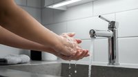 Hands washing under running water from modern chrome faucet in clean bathroom sink. Personal hygiene and cleanliness routine in contemporary home interior.