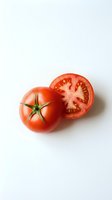 Fresh ripe tomato whole and sliced in half showing seeds and interior on white background, isolated for food and cooking design use.