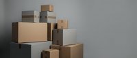 Stack of cardboard and white shipping boxes piled against a gray wall, representing moving, delivery, storage, or e-commerce logistics.