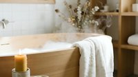 Wooden bathtub with white towel draped over edge, lit candle, dried flowers in vase, minimalist spa bathroom interior design for relaxation and wellness.