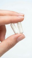 Hand holding two white capsules pills between fingers on clean white background for healthcare and medical supplement concepts.
