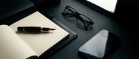Elegant dark office desk with open notebook, fountain pen, glasses, and smartphone, conveying professionalism and productivity.