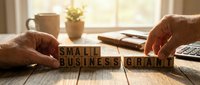 Small business grant concept with wooden blocks spelling the words on a desk with calculator and notebook in background.