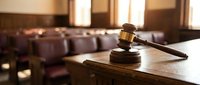 Wooden gavel and sound block on judge bench in empty courtroom with warm lighting. Legal justice system concept for law firm presentations.