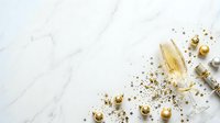 Champagne flute with golden spheres and star confetti on white marble surface, celebration and festive party styling for holiday events and special occasions.