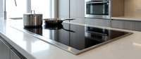 Modern kitchen with induction cooktop and stainless steel cookware on white countertop. Contemporary appliances and clean design for culinary cooking concepts.