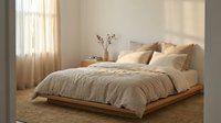 Minimalist bedroom with a low wooden platform bed, neutral linen bedding, soft natural light, and warm beige tones creating a calm, cozy interior.