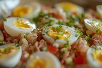 Fresh halved eggs with vibrant yolks garnished with chopped chives and bacon bits on bed of diced tomatoes, close up view showing texture and appetizing details.