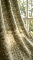 Neutral linen curtains drape elegantly beside a sunlit window, showcasing soft natural light filtering through woven fabric for home decor and interior design projects.