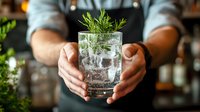 Professional bartender presenting craft gin cocktail with fresh rosemary garnish in elegant glass, premium mixology service for hospitality industry.