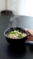 Steaming hot pho soup in a black bowl with bean sprouts, fresh basil, and lime, held by hand on a dark wooden table.