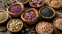 Assorted legumes and beans in wooden bowls on rustic burlap background. Healthy protein sources including lentils, chickpeas, kidney beans for cooking and nutrition.