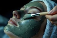 Young woman receiving green clay facial mask application with brush at spa salon, close up view of skincare treatment and beauty procedure.