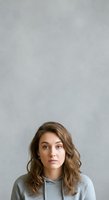 Young woman with wavy brown hair wearing gray hoodie against neutral background, suitable for portrait, lifestyle, and casual apparel marketing.