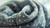 Soft gray polka dot fabric creates elegant swirls and folds in macro photography, showing delicate textile texture and pattern detail in natural light.