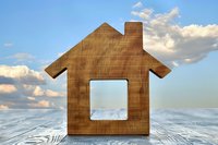 Wooden house silhouette on rustic table against cloudy sky background. Minimalist home symbol with window cutout represents real estate and property concepts.