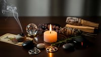 Mystical altar setup with burning candle, incense smoke, tarot cards, crystals, pentagram symbols and ritual objects for spiritual practices.