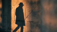 Mysterious silhouette of man in hat and coat casting dramatic shadow on textured wall during golden hour lighting for noir detective stories.